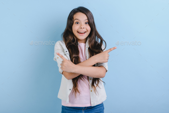 Excited young girl pointing her index finger right and left with crossing hands.