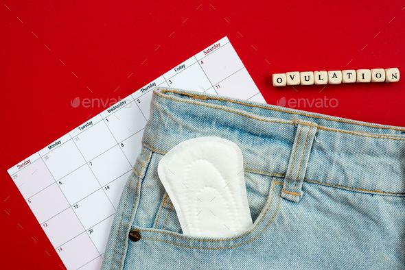 Tracking the menstrual cycle and ovulation. on a red background women\'s pads in jeans pocket.