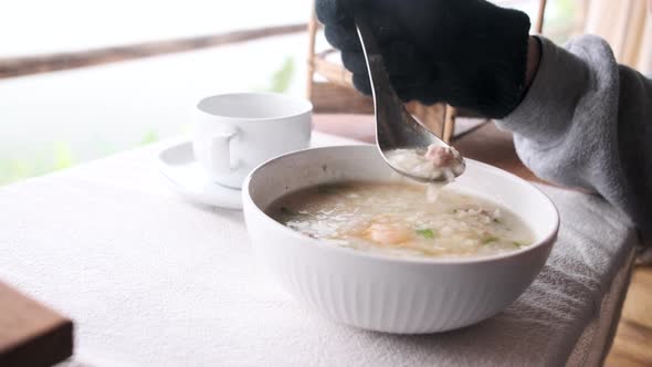 A woman eats a cup of hot congee, pork, and boiled egg in the winter morning. alt