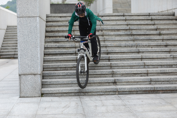 Woman free rider riding bike going down city stairs