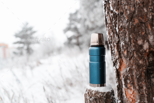 Camping vacuum flask and winter wood. Thermos standing on a stump. Travel concept