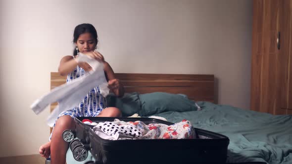 Front View of Young Woman Enjoys Folding Baby's Onesie and Placing It Into the Luggage alt