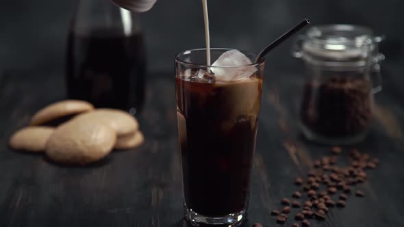 Slow Motion of Cream Being Poured Into a Tall Glass of Cold Brew Iced Coffee on Black Wood Table