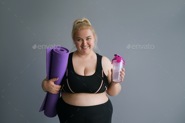 Plus Size blonde woman holding pilates mat and water bottle.