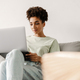 Young black woman working with laptop while sitting on couch at home - PhotoDune Item for Sale