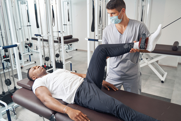 Experienced physiotherapist applying gym equipment for patient leg