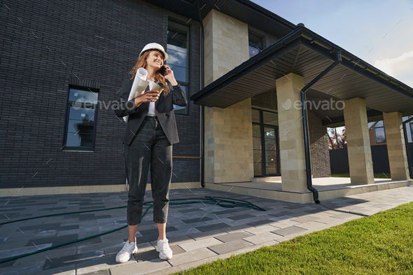 Happy woman engineer having a call in front of house