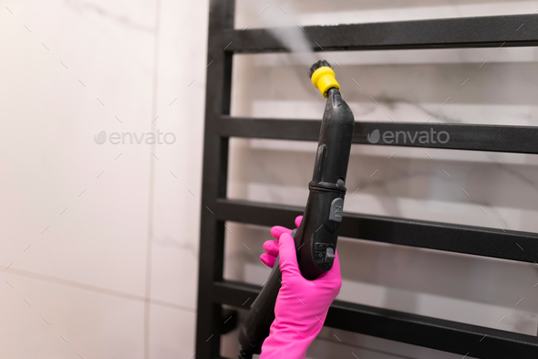 Woman doing steam cleaning of bathroom towel radiator. Heated towel rail clean process