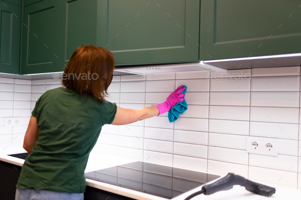 Woman wipes tiles in the kitchen. Cleaning employee cleans the house