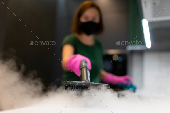 Woman employee cleaning company blows vapor out of steam generator.