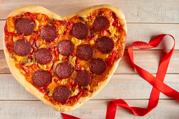 Heart shaped pepperoni pizza on a wooden background. Valentines day gift