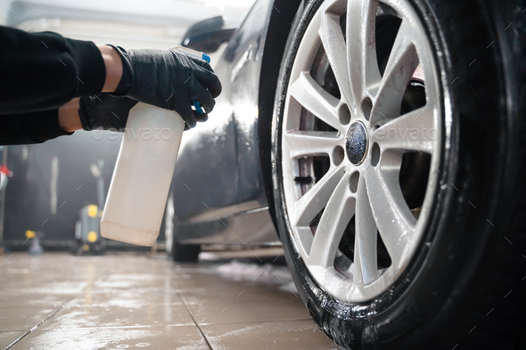 Auto detailing worker applies chemistry to wheels. Professional car wheel wash