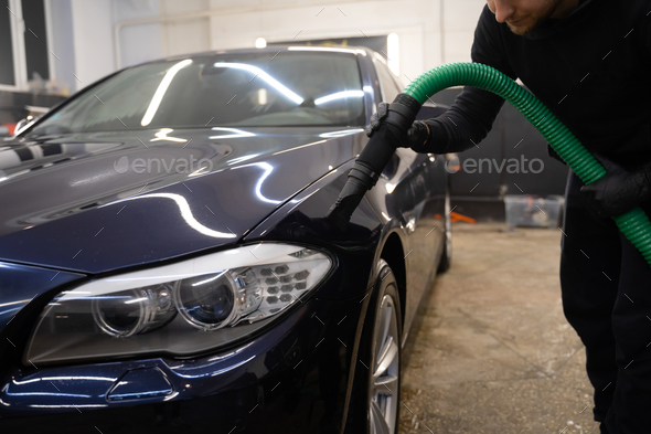 Car drying process after washing. Man with vacuum cleaner removes water droplets from car.