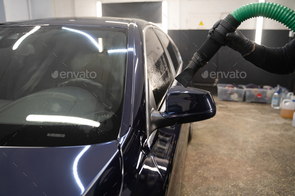 Car drying process after washing. Man with vacuum cleaner removes water droplets from car.