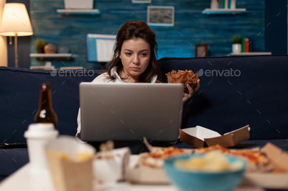 Influencer checking social media on laptop eating a tasty takeout burger and fast food delivery menu