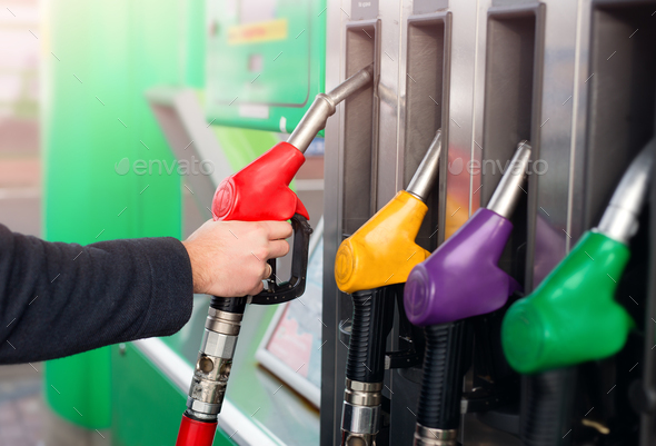 Closeup of male hand holding gas red pump nozzle . Gas station