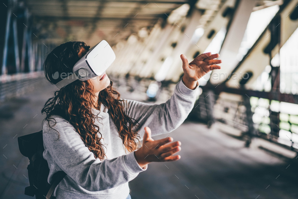 woman in virtual reality glasses with backpack walks under bridge