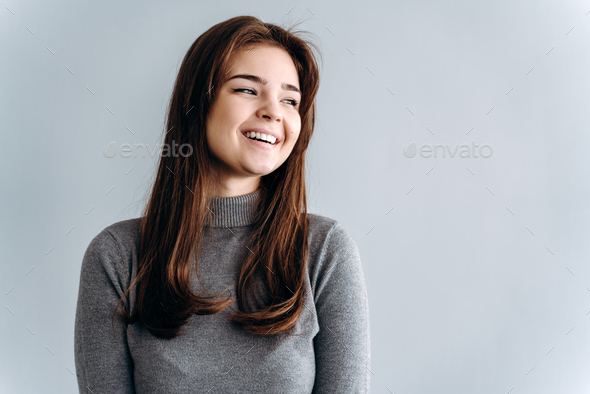 Charming, smiling girl on a gray background stands. Studio shooting, blank wall