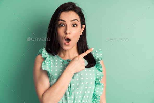 Surprised brunette and polka dot dress with index finger on copy space.