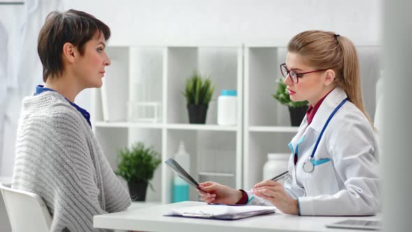 Young Female Practitioner Consultation Mature Woman Patient Looking on Xray Image alt
