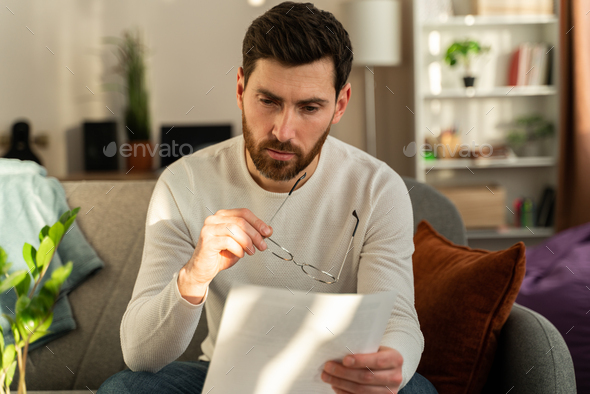 Frustrated millennial guy holding glasses and reading bad unpleasant news in postal letter