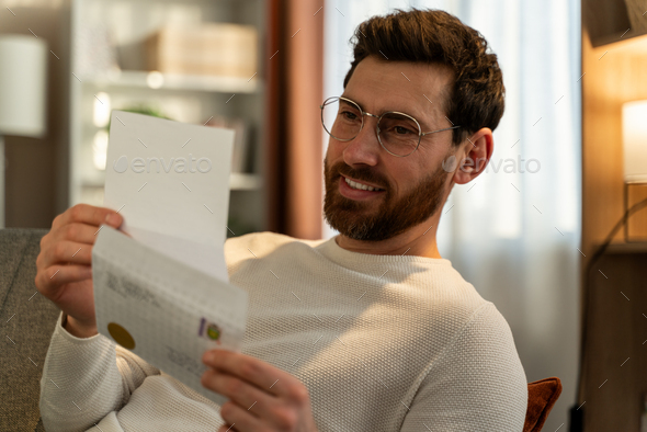 Millennial guy wearing glasses reading pleasant news in postal letter