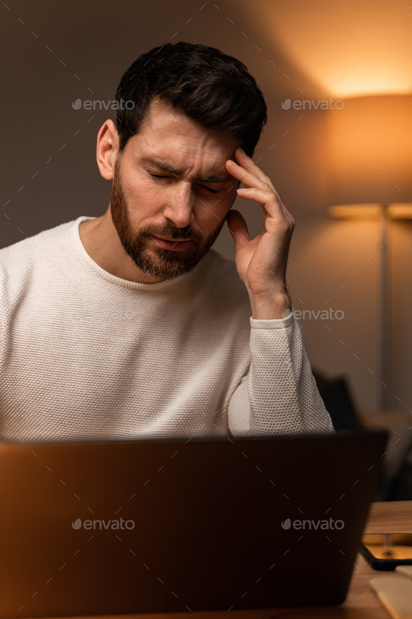 Tired caucasian man suffering from headache bad vision sight problem sitting at table using laptop