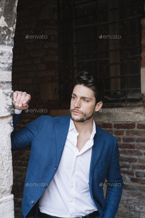 Elegant man at old brick building looking around Stock Photo by westend61