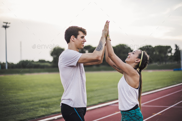 Male and female athlete high fiving on a tartan track