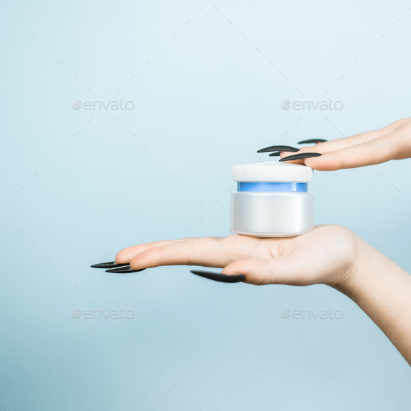 Female hands hold jar of cream on light blue background. Blank surface for logo, mock up. Cosmetics