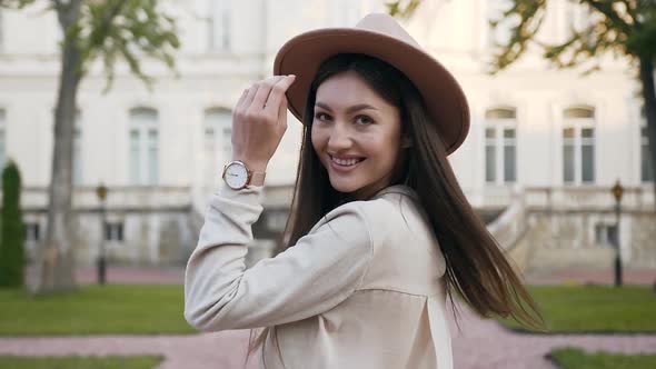 Woman with Long Hair and Fashion Hat which Turning and Looking at Camera while Walking alt