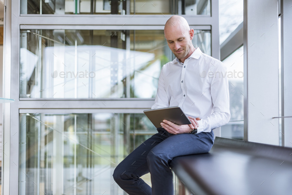 Smiling businessman sitting at the window using tablet - Stock Photo - Images