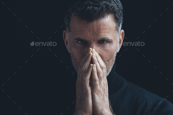 Portrait of man covering mouth with his hands in front of black background