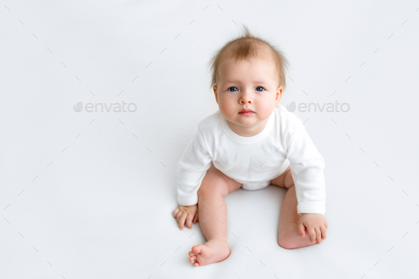 Infant with protruding hair is sitting looking at the camera.