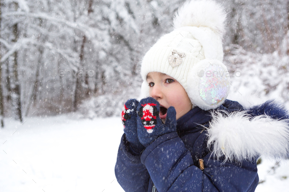 A little girl in the cold warms her hands in mittens-breathes warm air from her mouth on her hands