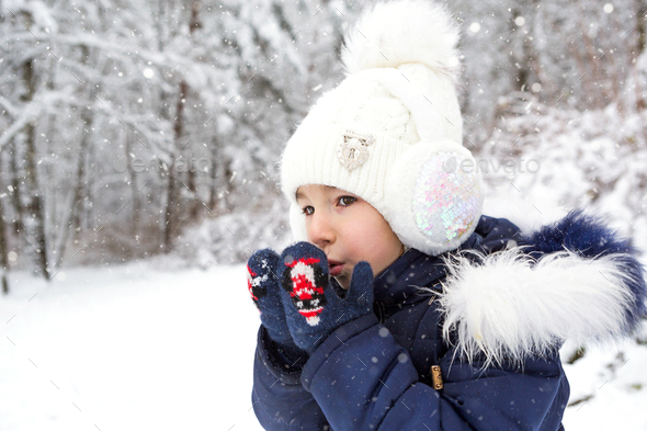 A little girl in the cold warms her hands in mittens-breathes warm air from her mouth
