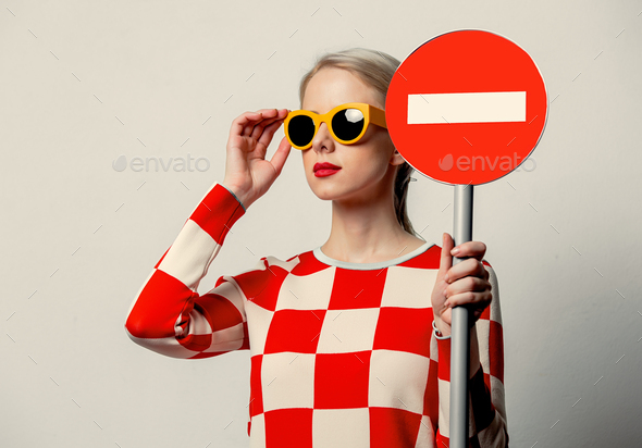 Beautiful woman with blond hair in in a 70s red square dress with no entry sign
