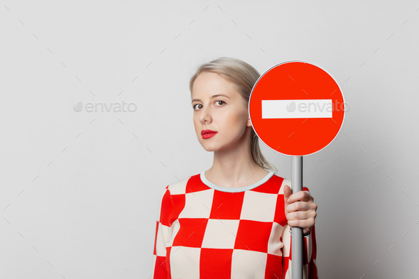 Beautiful woman with blond hair in in a 70s red square dress with no entry sign