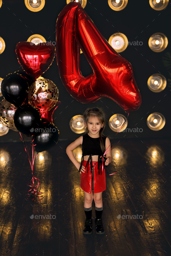A girl dressed in rock style stands with a balloon in the shape of the number four