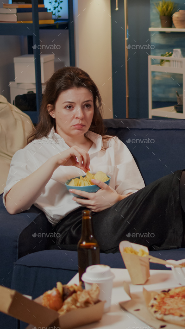 Young woman laying on couch holding bowl of chips