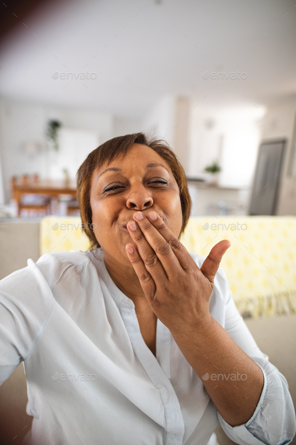 Happy african american senior woman blowing kiss during video call at home