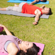 Young woman lying on exercise mat with eyes closed while practicing yoga with people in park - PhotoDune Item for Sale