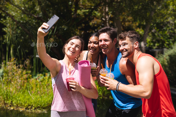 Happy male and female friends taking selfie while holding healthy drinks post workout in park