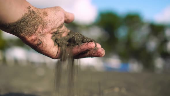 close-up hand grabs a handful of dry sand and lets it fall between his fingers alt
