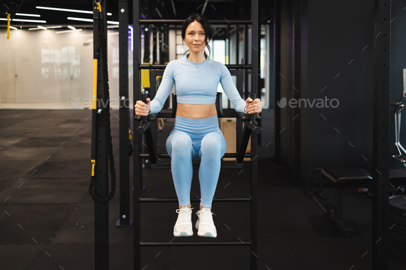 Athletic woman shakes her lower abdomen on uneven bars in the gym