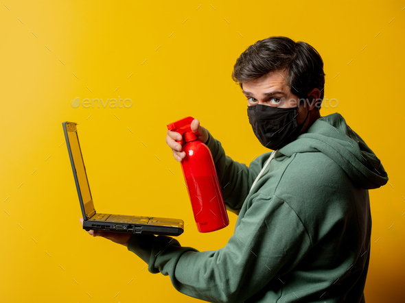 guy in facemask hold disinfection spray and notebook on yellow background