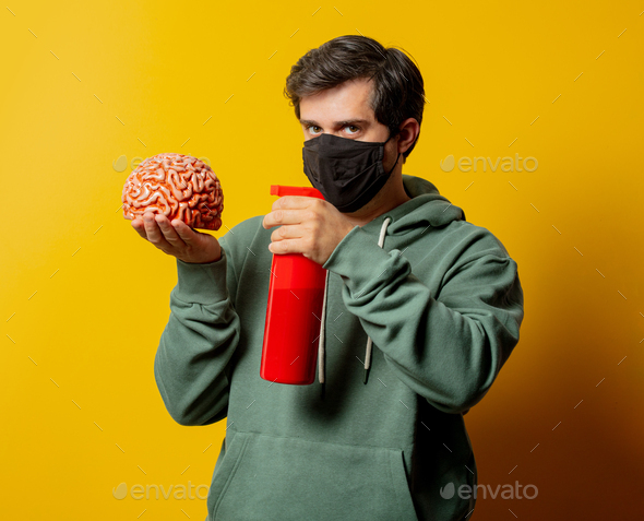 guy in facemask hold disinfection spray and human brain on yellow background
