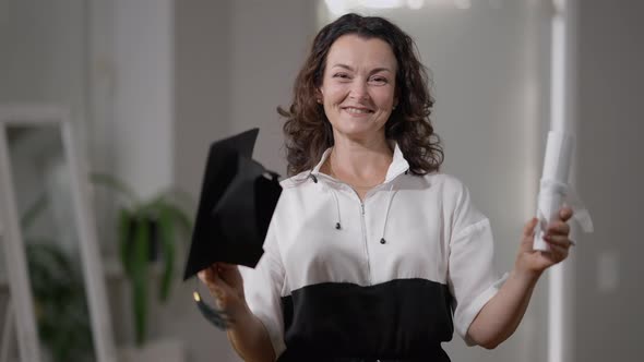 Portrait of Smiling Joyful Caucasian Mature Woman Posing with Graduation Cap and Rolled Diploma alt