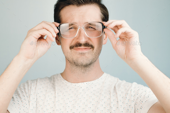 Young man in big glasses squints at the camera, close-up. Health problem concept, low vision