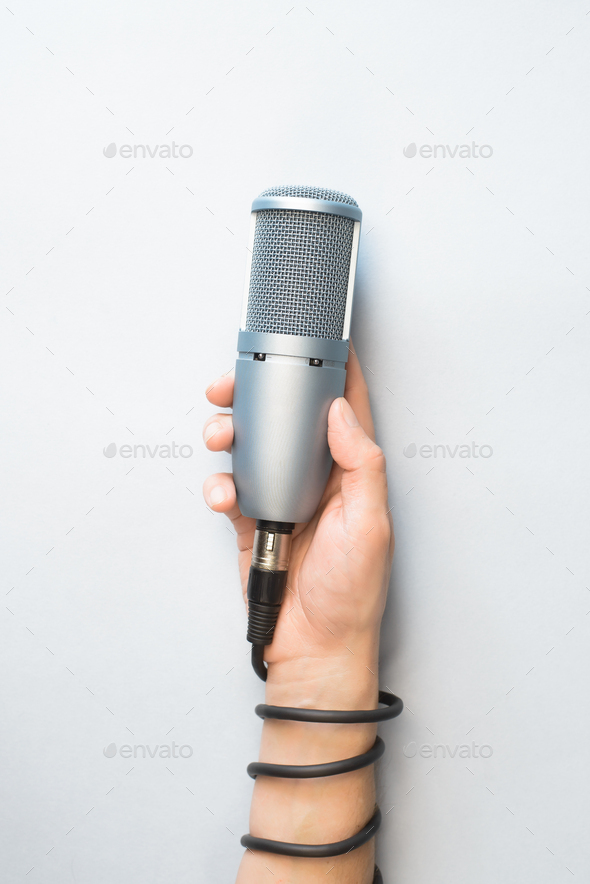 Male hand holding professional microphone on light background, top view. The microphone cable